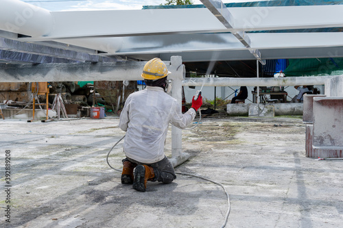 The painter is working to fireproof paint on steel structure with spray gun, at industrial factory.