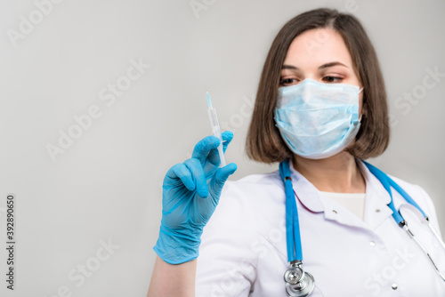 Portrait of young beautiful doctor shows syringe in hands on light background