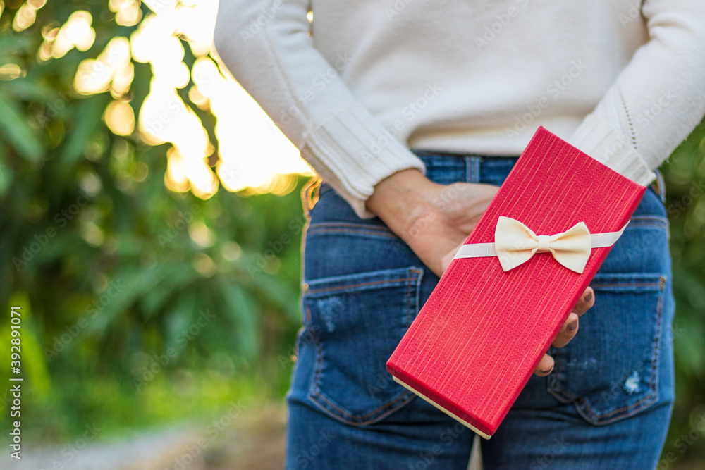 Woman's hand holding gift red box on green natural blur background.