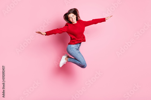 Full length body size portrait of pretty funny girl jumping high wearing casual clothes smiling keeping hands like plane isolated on pink color background