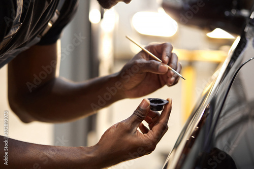 african man's hands use the detail brush to paint car or to clean and remove the dirt, car detailing and car wash painting concept. close-up, cropped male