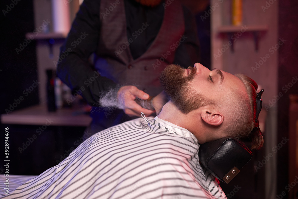 Fototapeta premium modern barber male begins to cut hair of client, making stylish beard, hair cut in salon