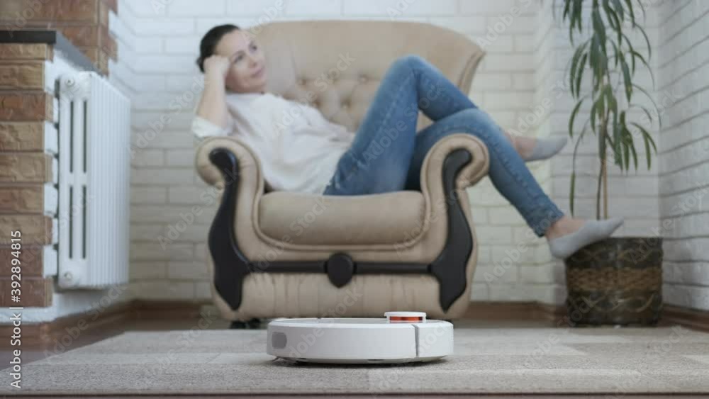 Relaxing with a robot vacuum cleaner. The female is resting in the chair, the smart vacuum cleaner is working. Relaxing with a robot vacuum cleaner. The female is resting in the chair, the smart vacuum cleaner is working.