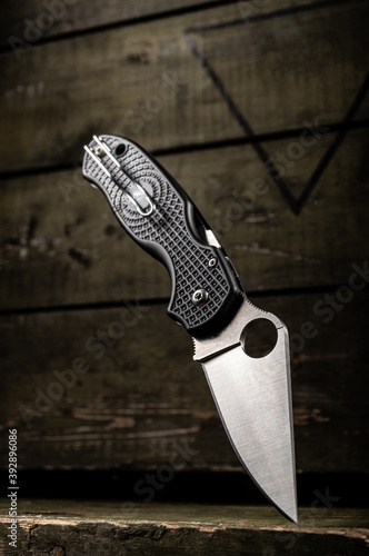 Knife with a hole in the blade. Wire clip for carrying knife. Military wooden box on the background. photo