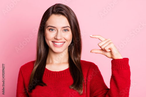 Photo portrait of funny pretty girl showing small size measures with fingers smiling isolated on pink color background