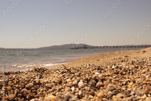 A low view of the rocky sandy beach of the Black Sea Bourgas Bay with the Bridge blurry in the background and small pebbles in the foreground defocused blurry in a sunny day in Bulgaria on May 2020 