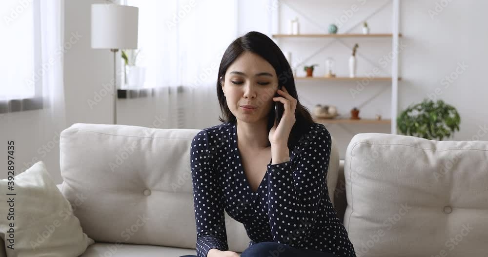 Happy pretty young korean vietnamese woman resting on comfortable sofa, involved in mobile phone call conversation, discussing life events with friends or family distantly, talking chatting indoors. Happy pretty young korean vietnamese woman resting on comfortable sofa, involved in mobile phone call conversation, discussing life events with friends or family distantly, talking chatting indoors.