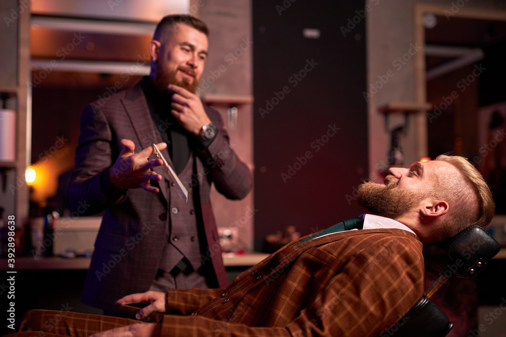 male barber is ready to cut his client sitting on chair wearing formal suit, professional caucasian barber ready to do a trendy haircut