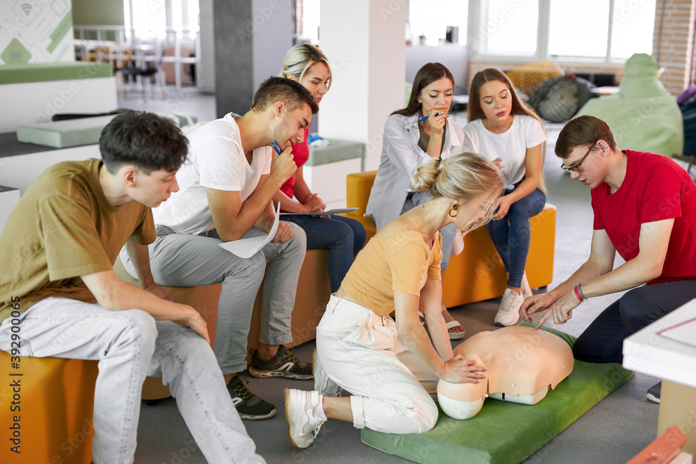 Obraz premium CPR class with male instructor speaking and demonstrating help, giving lessons of first aid. compression and resuscitation procedures. Cpr mannequin is used for an example