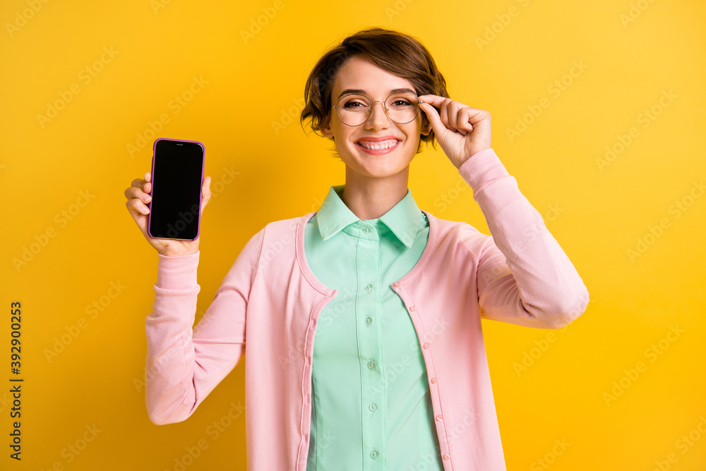 Photo portrait of happy girl in eyeglasses showing cellphone touchscreen copyspace isolated on vibrant yellow color background Photo portrait of happy girl in eyeglasses showing cellphone touchscreen copyspace isolated on vibrant yellow color background