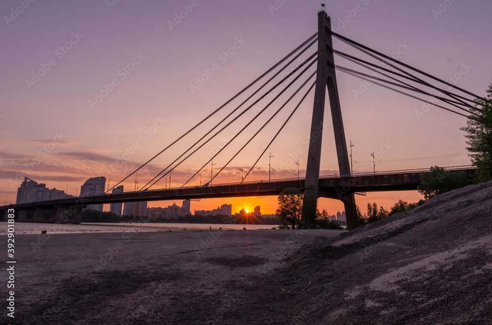 Large cable-stayed bridge over the river. Sunset behind the bridge.