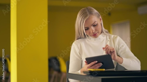 Young woman sitting at her desk she's drawing, writing and using pen with digital tablet computer. Girl using tablet working in office browsing information looking at data on digital touchscreen.