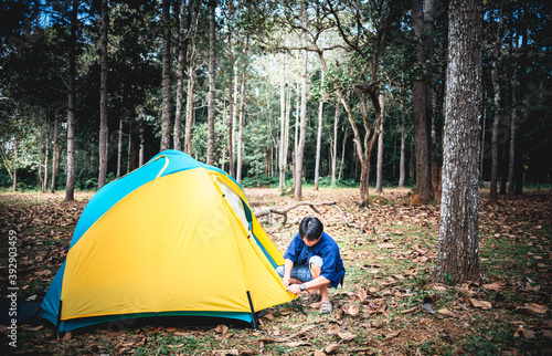 An Asian male tourist, Pitch a yellow tent for Camping in a forest with tall trees, to people and travel concept.