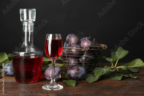 Delicious plum liquor and ripe fruits on wooden table against black background. Homemade strong alcoholic beverage