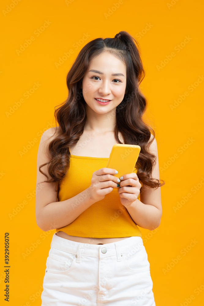 Focused curly woman texting message. Studio shot of elegant girl holding smartphone on yellow background. Focused curly woman texting message. Studio shot of elegant girl holding smartphone on yellow background.
