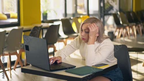 A tired young woman is working using her laptop computer. Sleepy girl falls asleep at workplace. Boring female trying to work at coworking. Sleeping woman work in business office.