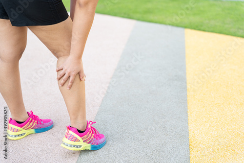 Female fatty runner athlete leg injury and pain. Hands grab painful leg while running in the park.