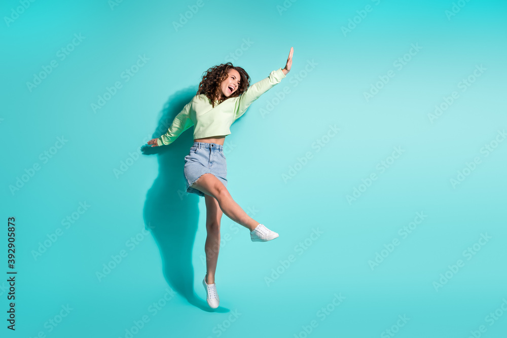 Full length body size photo of brunette girl dancing jumping keeping hand up singing isolated on vibrant teal color background