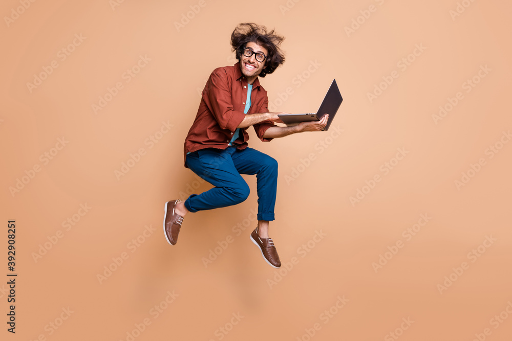 Full length photo portrait of excited guy jumping up with laptop in hands isolated on pastel beige colored background Full length photo portrait of excited guy jumping up with laptop in hands isolated on pastel beige colored background