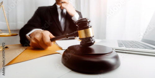 Justice and law concept.Male judge in a courtroom with the gavel, working with, computer and docking keyboard, eyeglasses, on table in morning light