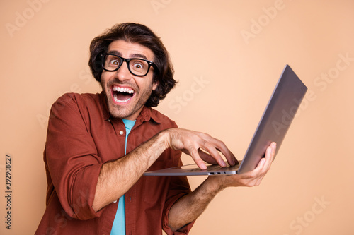Photo portrait of mad hacker typing holding laptop in hand isolated on pastel beige colored background