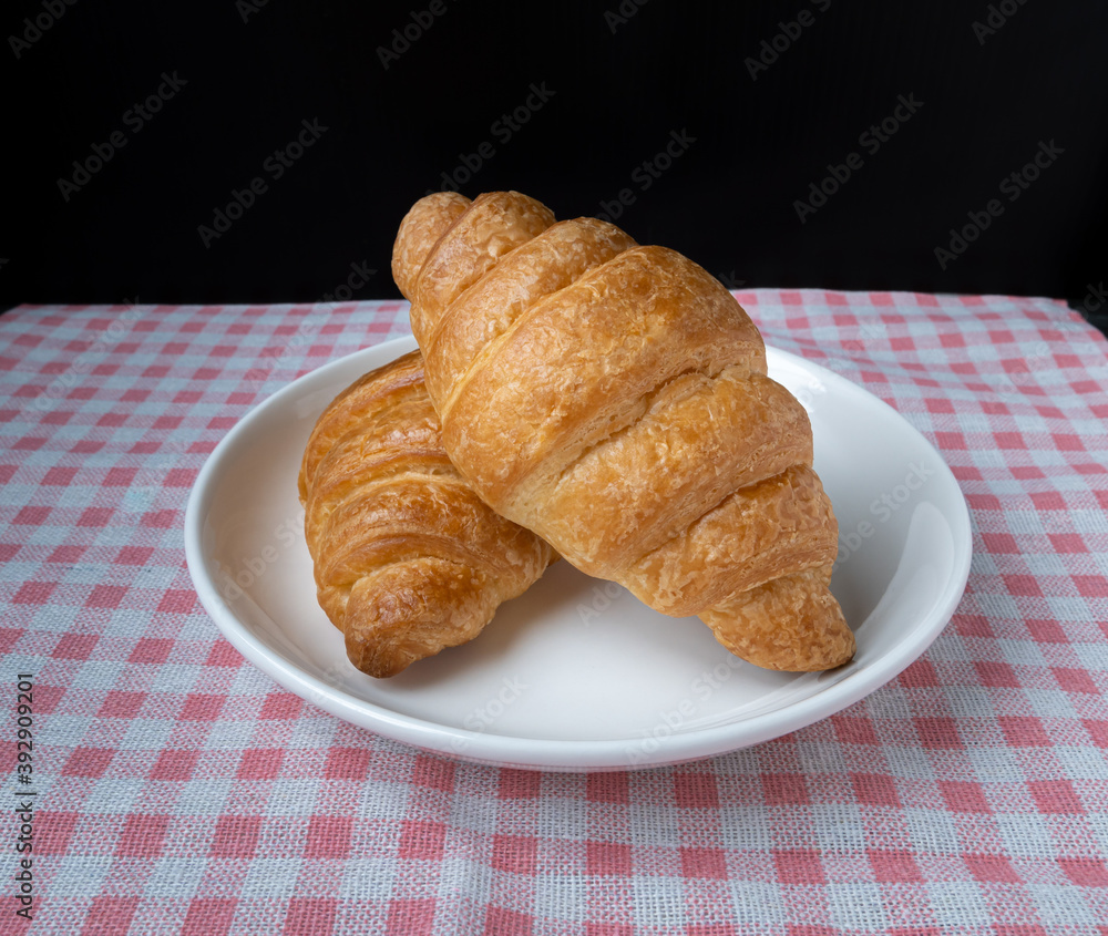 Delicious fresh croissants in Plate on pink Plaid pattern background. French breakfast. Tasty croissants with copy space Delicious fresh croissants in Plate on pink Plaid pattern background. French breakfast. Tasty croissants with copy space