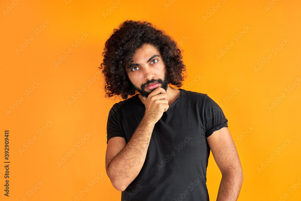 determined arabic male with beard is thinking and looking worried, standing against orange background. determined arabic male with beard is thinking and looking worried, standing against orange background.