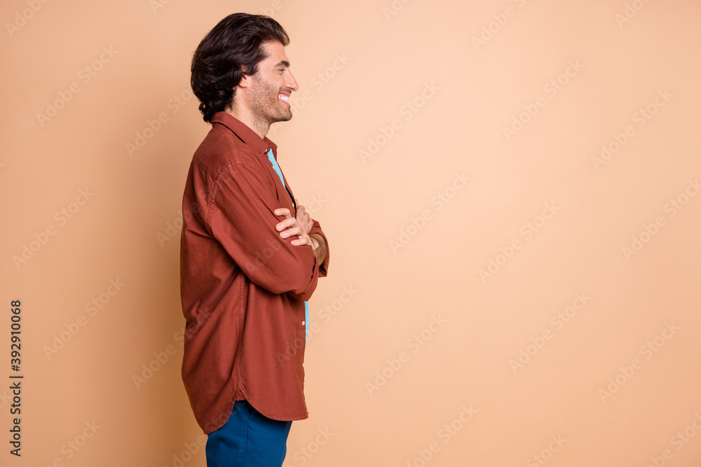 Profile photo of confident positive man folded arms look empty space wear brown t-shirt isolated beige color background Profile photo of confident positive man folded arms look empty space wear brown t-shirt isolated beige color background