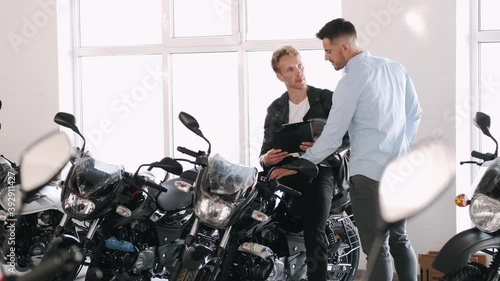 Handsome customer listening to motorcycle salon manager. The client is going to buy a motorbike. Dealership, sports shop. Biker lifestyle.