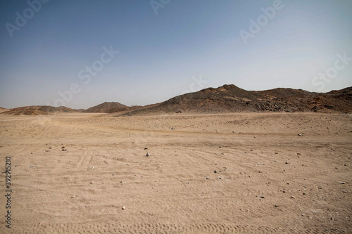 A view of a sandy desert with mountains and the pyramids in the background