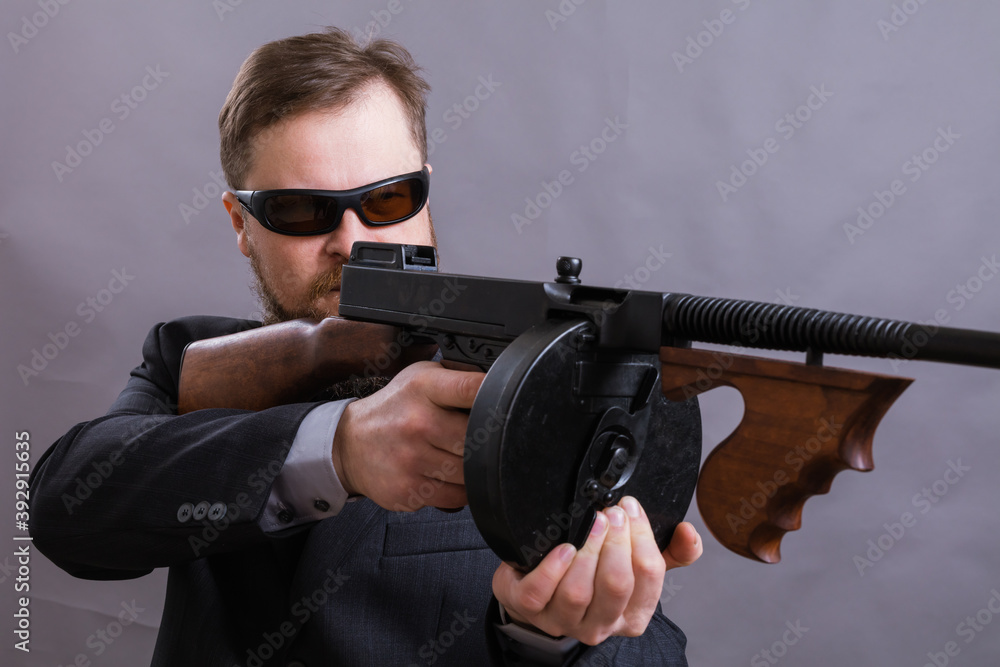 Mature man in sunglasses dressed in suit with tommy gun Mature man in sunglasses dressed in suit with tommy gun