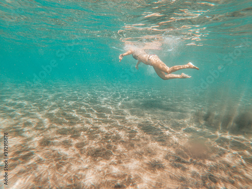 Underwater view in blue sea ocean water of active woman swimming and enjoying the summer holiday vacation at the beach