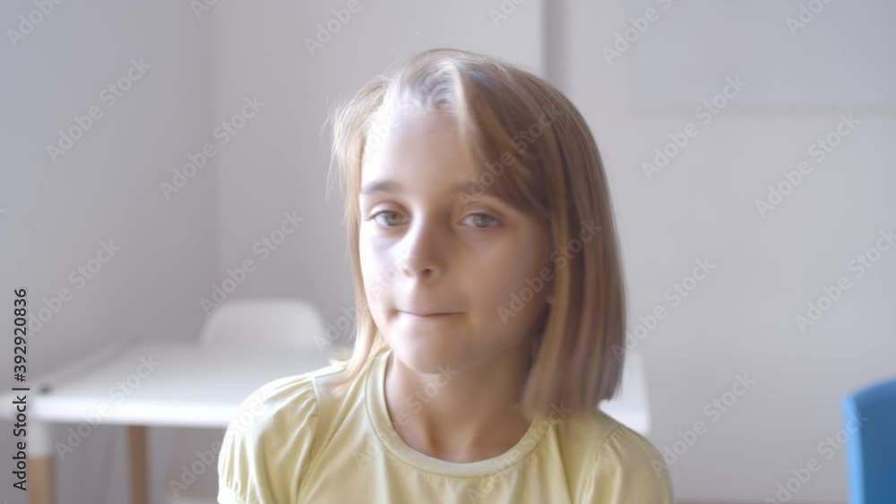 Positive pretty Caucasian girl standing in classroom, turning head away then looking at camera. Child portrait concept Positive pretty Caucasian girl standing in classroom, turning head away then looking at camera. Child portrait concept