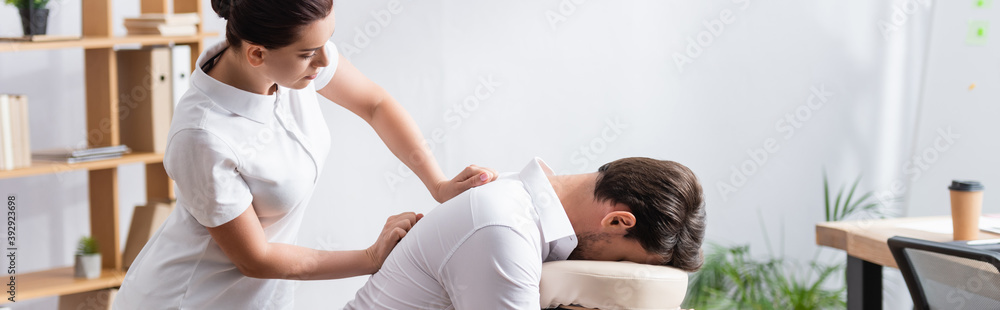 Εκτύπωση καμβά Side view of masseuse doing back massage for businessman in office, banner