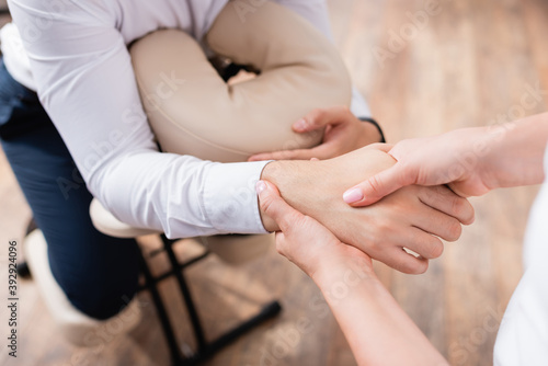 Cropped view of masseuse doing massage of businessman hand on blurred background