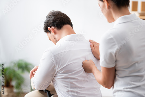 Masseuse massaging back of businessman sitting in office on blurred background