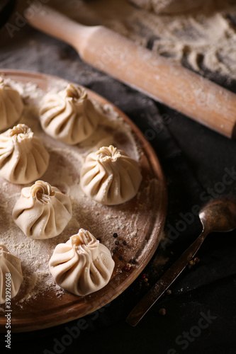 Georgian cuisine. Khinkali. Raw dough with minced meat on a wooden board with flour on a black table. Rolling pin, cooking process. Background image, copy space