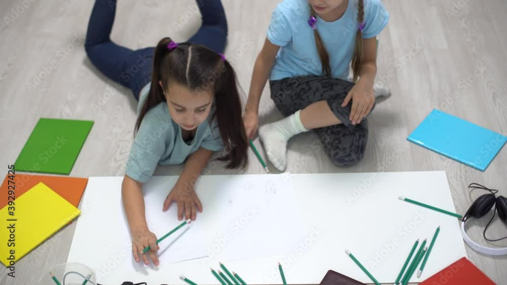 two little girls sisters lie on the floor of the house and draw with colored pencils on paper. children do creative homework after school. two little girls sisters lie on the floor of the house and draw with colored pencils on paper. children do creative homework after school.