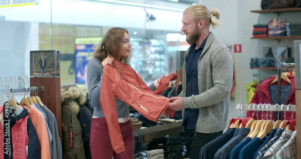 Beautiful young girlfriend asking boyfriend to buy coat in clothing shop. Handsome bearded man disagree with woman. Couple shopping during Black Friday sales. Cinema 4k ProRes HQ. Beautiful young girlfriend asking boyfriend to buy coat in clothing shop. Handsome bearded man disagree with woman. Couple shopping during Black Friday sales. Cinema 4k ProRes HQ.