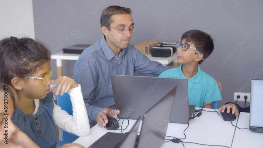 School boy sneezing during class. Teacher sitting at desk near children, explaining lesson and yawning while group using laptops. Digital education or virus at school concept School boy sneezing during class. Teacher sitting at desk near children, explaining lesson and yawning while group using laptops. Digital education or virus at school concept
