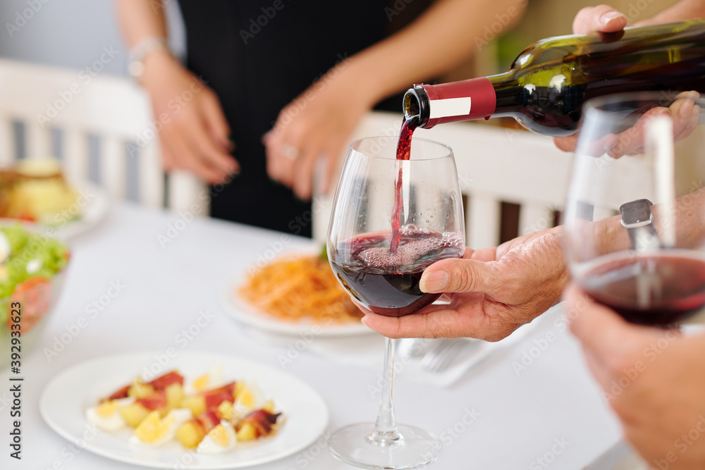 Person pouring red wine in glass for guest at house party