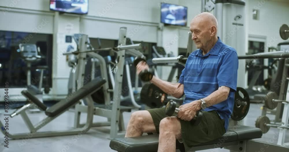 Elderly man lifts two dumbbells at gym, medium shot Elderly man lifts two dumbbells at gym, medium shot