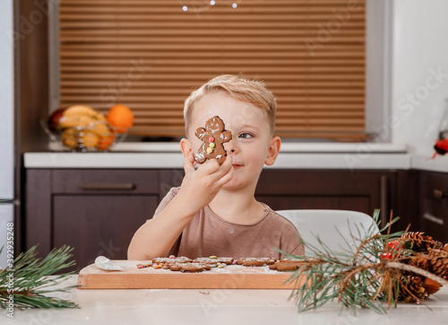 Boy holding a tray full of homemade gingerbread cookies. Kids bake Christmas cookies. Horizontal view of naughty little caucasian kid eating a bite of a chocolate ginger Christmas cookie.