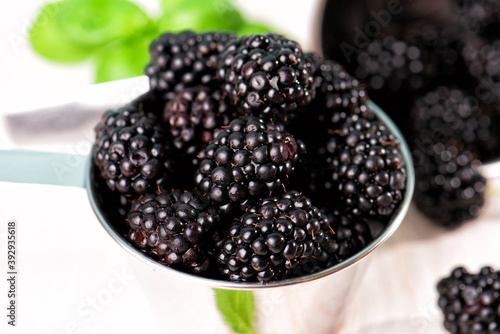 Ripe blackberries with basil leaves in a metal bowl on a wooden table