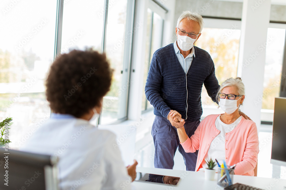 Senior couple with protective facial masks receive news from black female doctor Senior couple with protective facial masks receive news from black female doctor