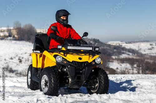 Young man driver on the ATV 4wd quad bike stand in heavy snow with deep wheel track. Moto winter sports