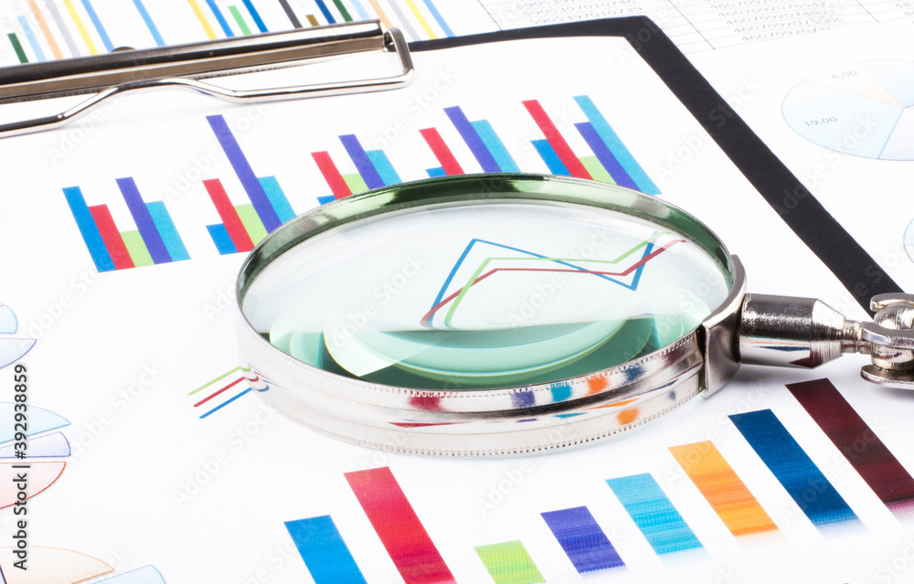 Magnifying glass lying on business charts and graphs. Business planning,accounting,analysis,financial planning and data Analysis concept. Magnifying glass lying on business charts and graphs. Business planning,accounting,analysis,financial planning and data Analysis concept.