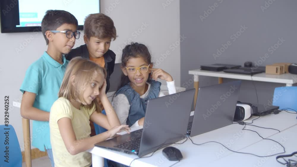 Naughty children sitting and standing at desk with laptops, watching and discussing content, teasing each other. Digital education concept Naughty children sitting and standing at desk with laptops, watching and discussing content, teasing each other. Digital education concept