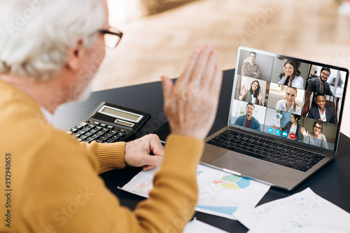 Video conference. Business partners communicate via video conference using laptop. The old gray-hair man talks with his business partners and waving hand. Distant work