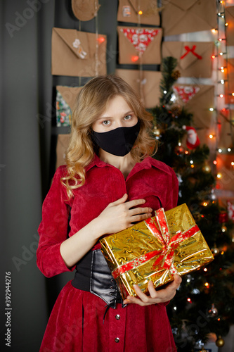 Portrait of a beautiful girl in medical mask, standing in front of decorated christmas tree at home